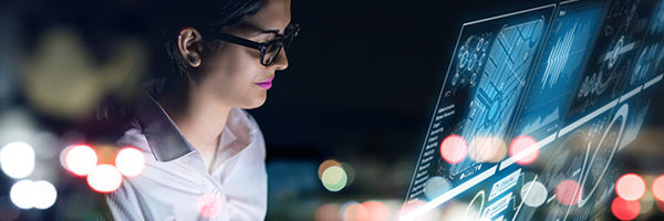 Een IT-vrouw zit in een IT-kantoor en kijkt naar een virtueel scherm met out-of-the-box dashboards van apparaatanalyses.